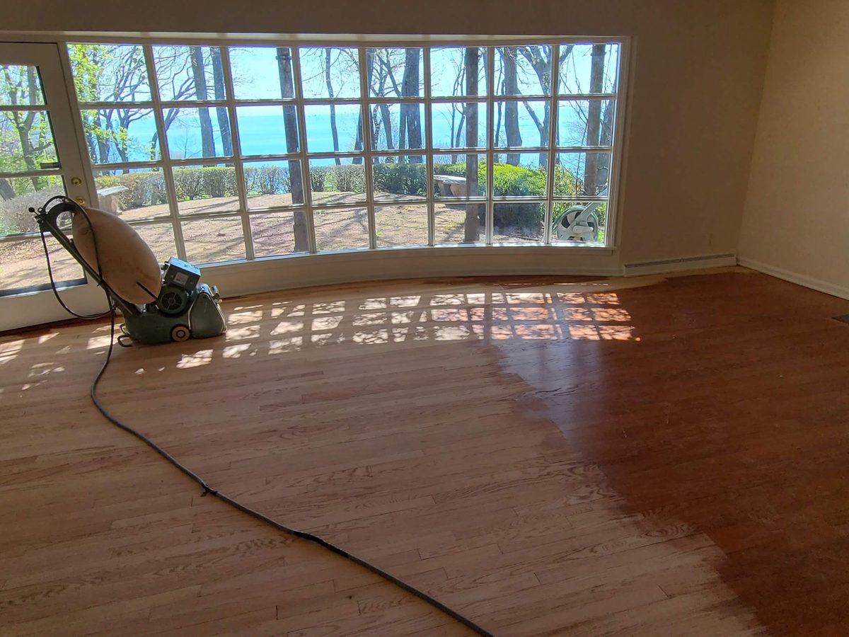 Drum sander cutting through old finish on a red oak living room floor in Fox Point